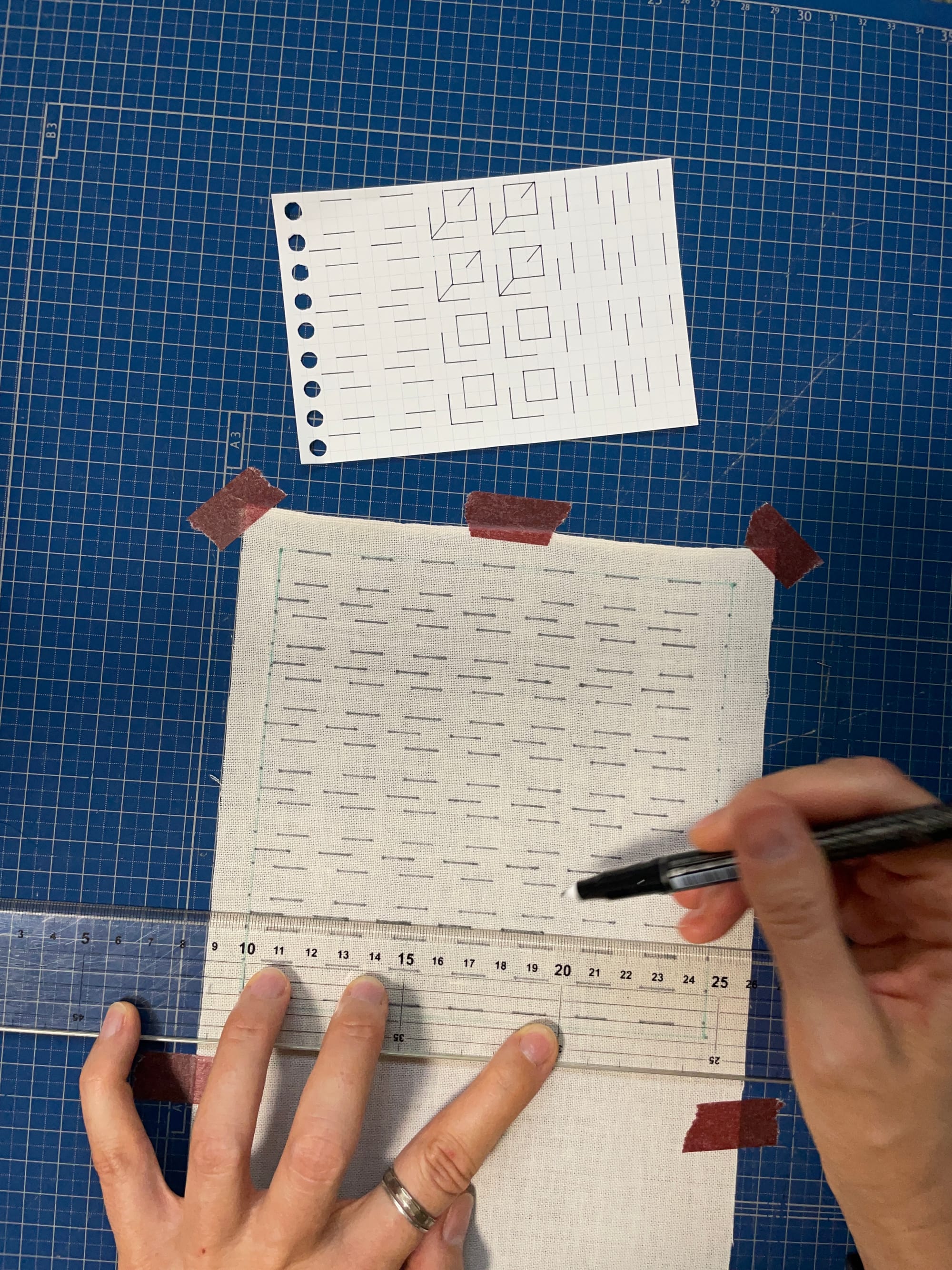 Two hands drawing black straight lines onto fabric