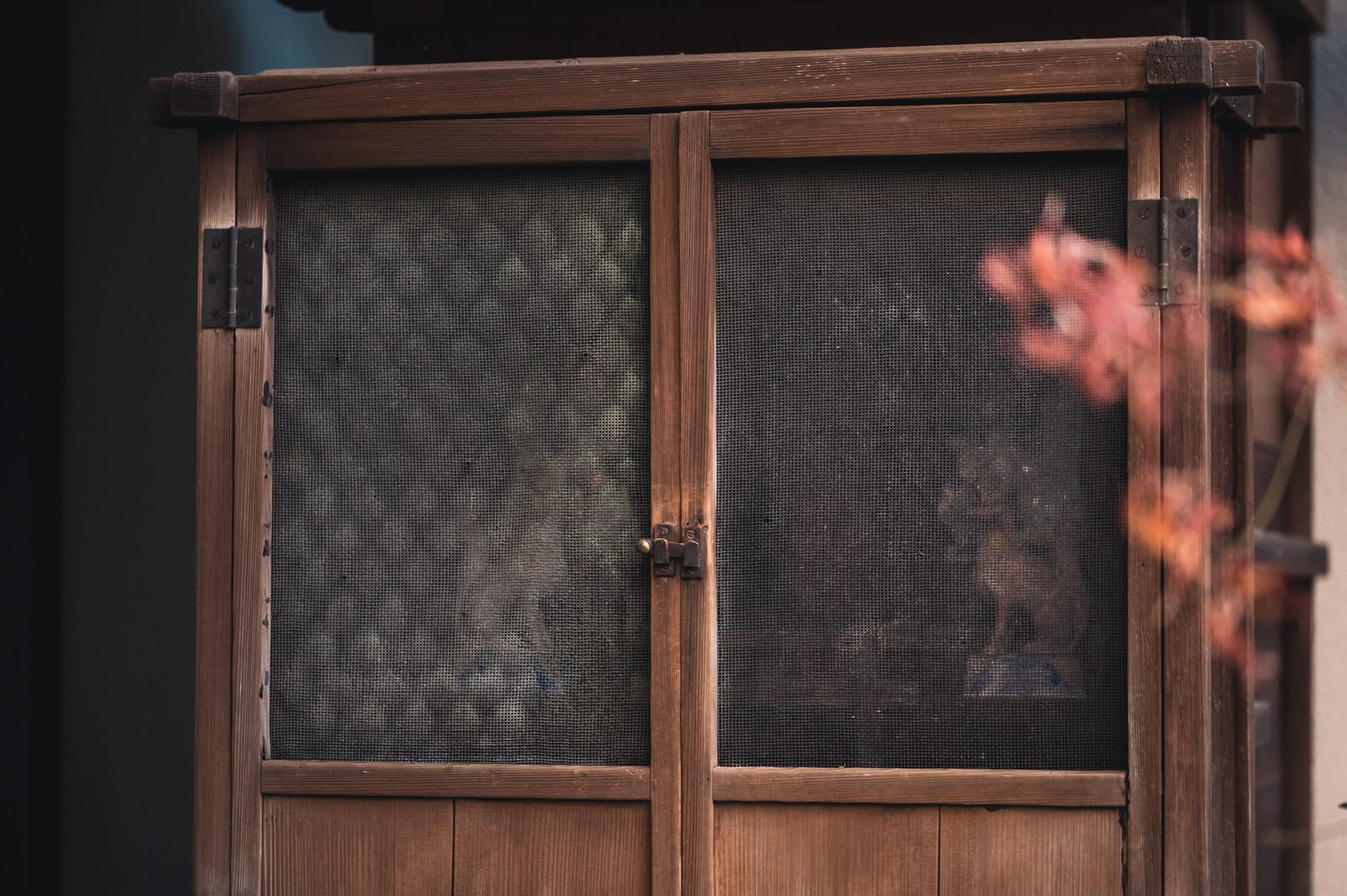 A wooden shrine where wooden fox statues can be seen behind a door with mesh