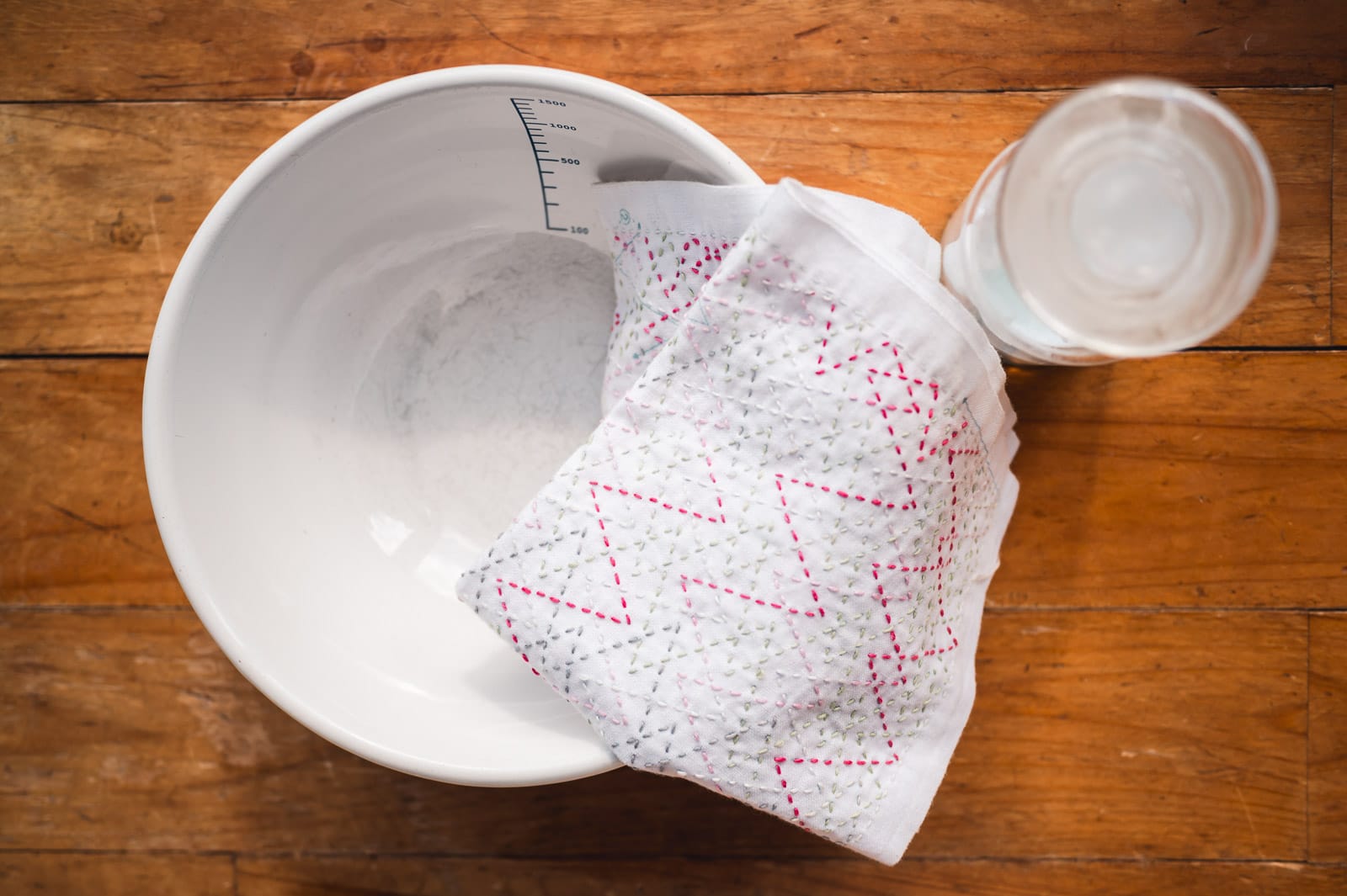 An enamel bowl with a dish cloth draped across its edge and a bottle with washing detergent next to it