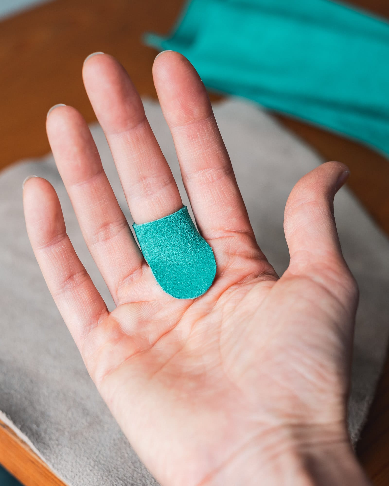 Green leather palm thimble worn on middle finger