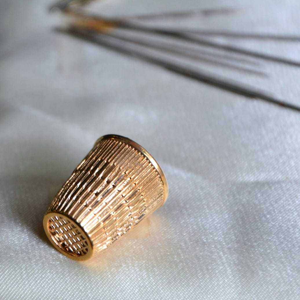 A golden metal thimble that is meant to be worn on the first joint of a finger.