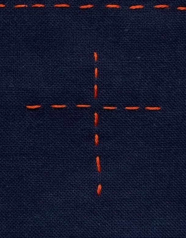 Indigo fabric with red sashiko stitches forming a cross, the intersection left blank