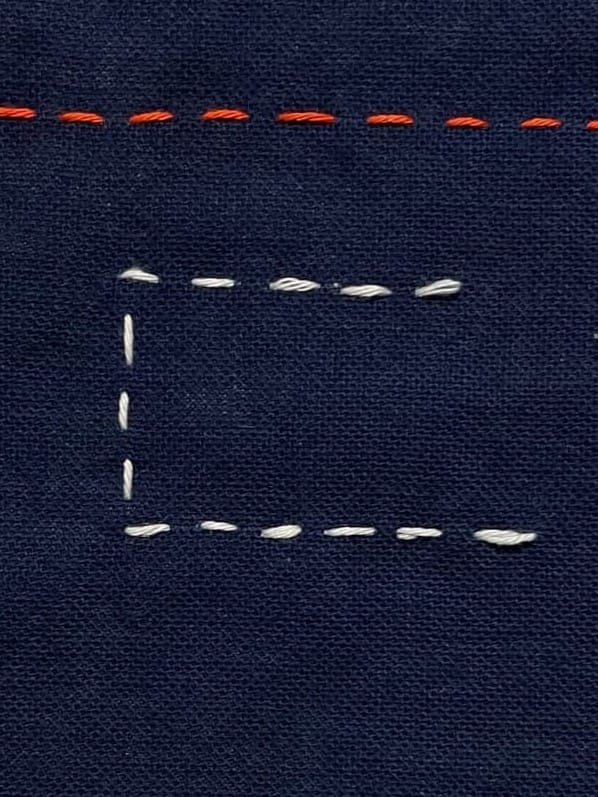 Indigo cloth with red and white sashiko stitches illustrating how to achieve sharp looking corners