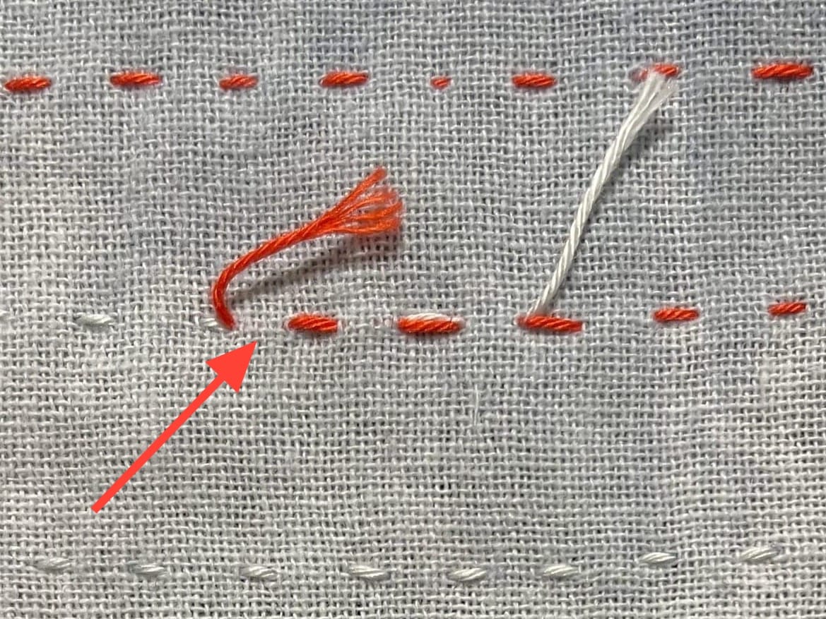 White fabric with red and white sashiko stitches illustrating how to connect threads when you run out of thread