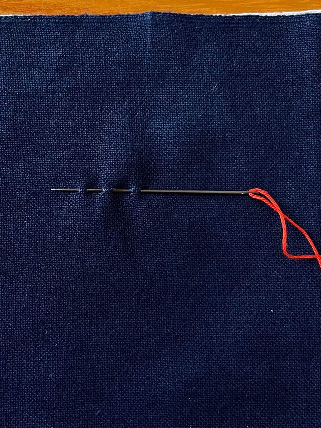 Indigo fabric with a needle and red thread sticking in the fabric