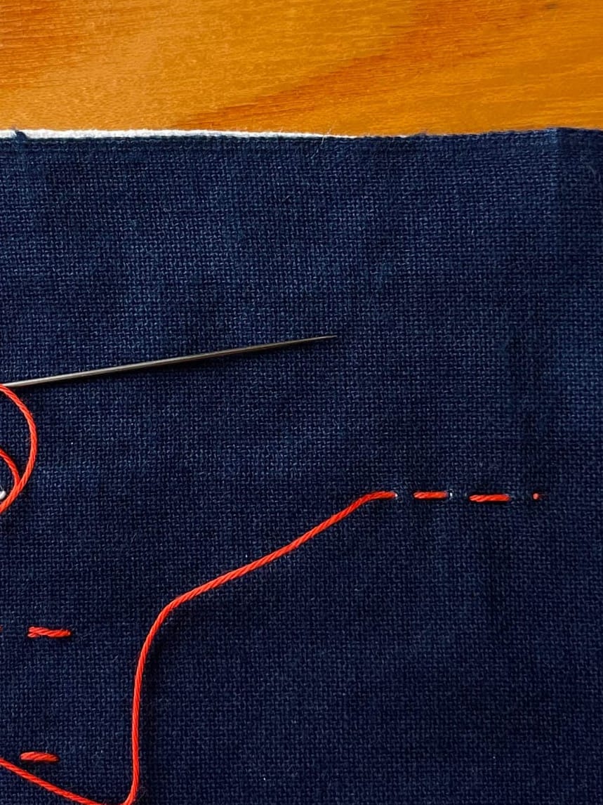 Indigo fabric with three stitches in red thread