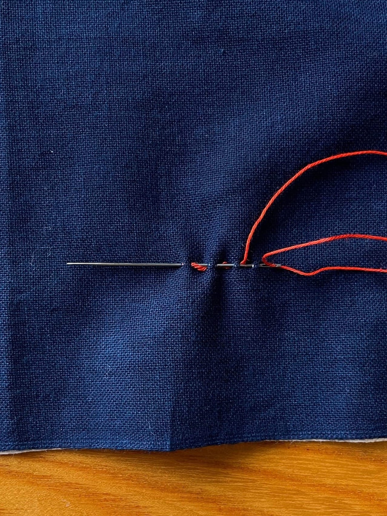 Indigo fabric and a needle gathering stitches and red thread 