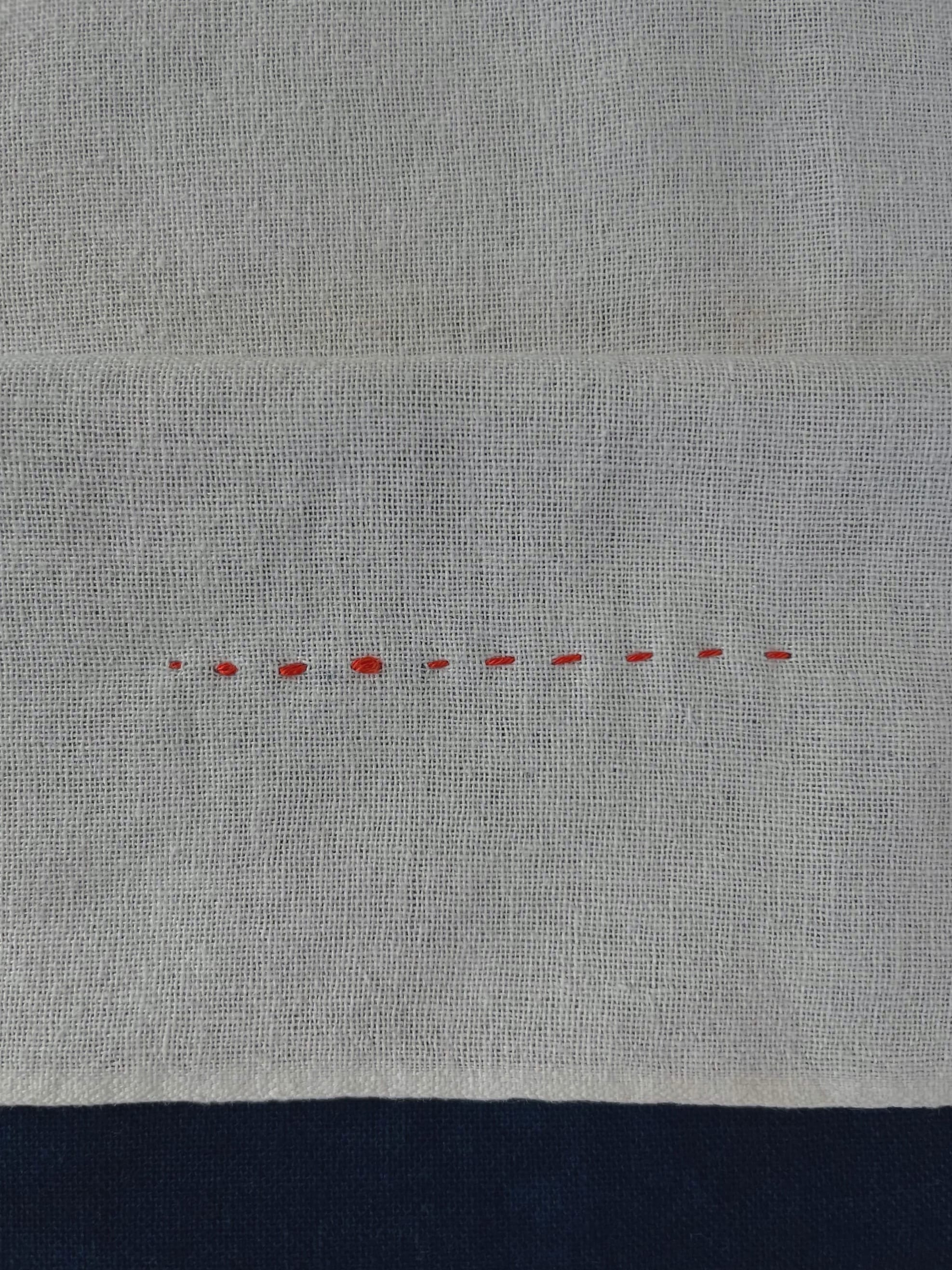 The wrong side of white fabric showing sashiko stitches in red