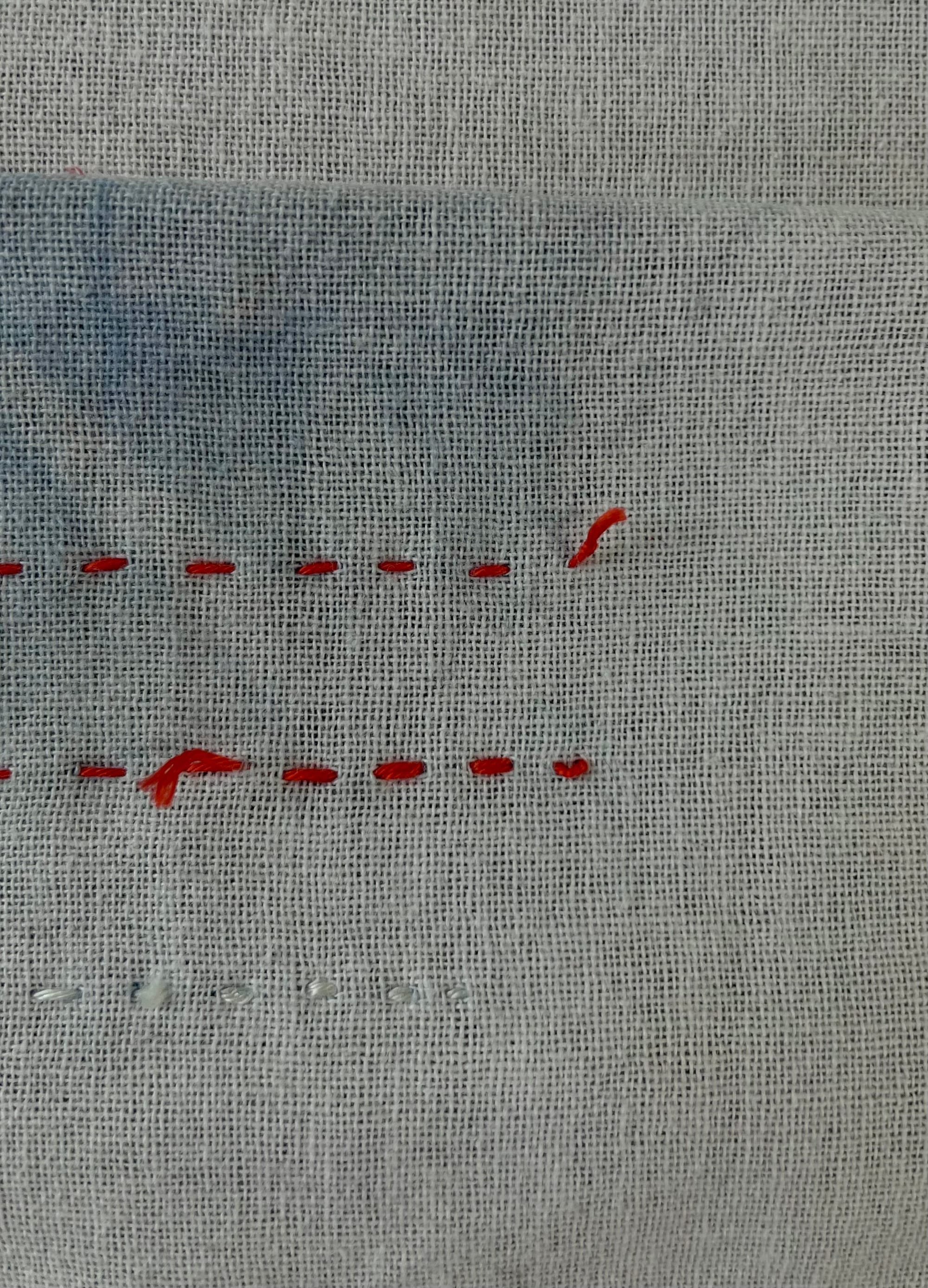 Wrong side of white sashiko fabric with stitches in white and red