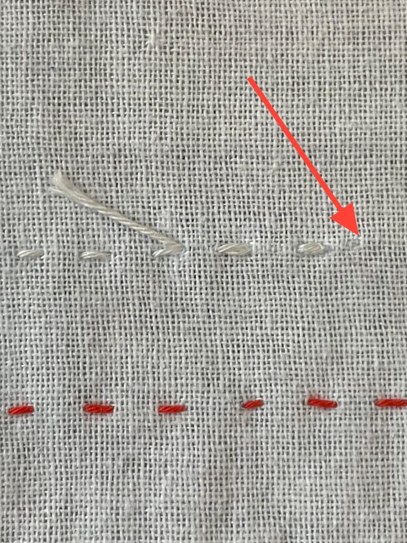 White sashiko fabric with stitches in red and white to show how to end stitches.