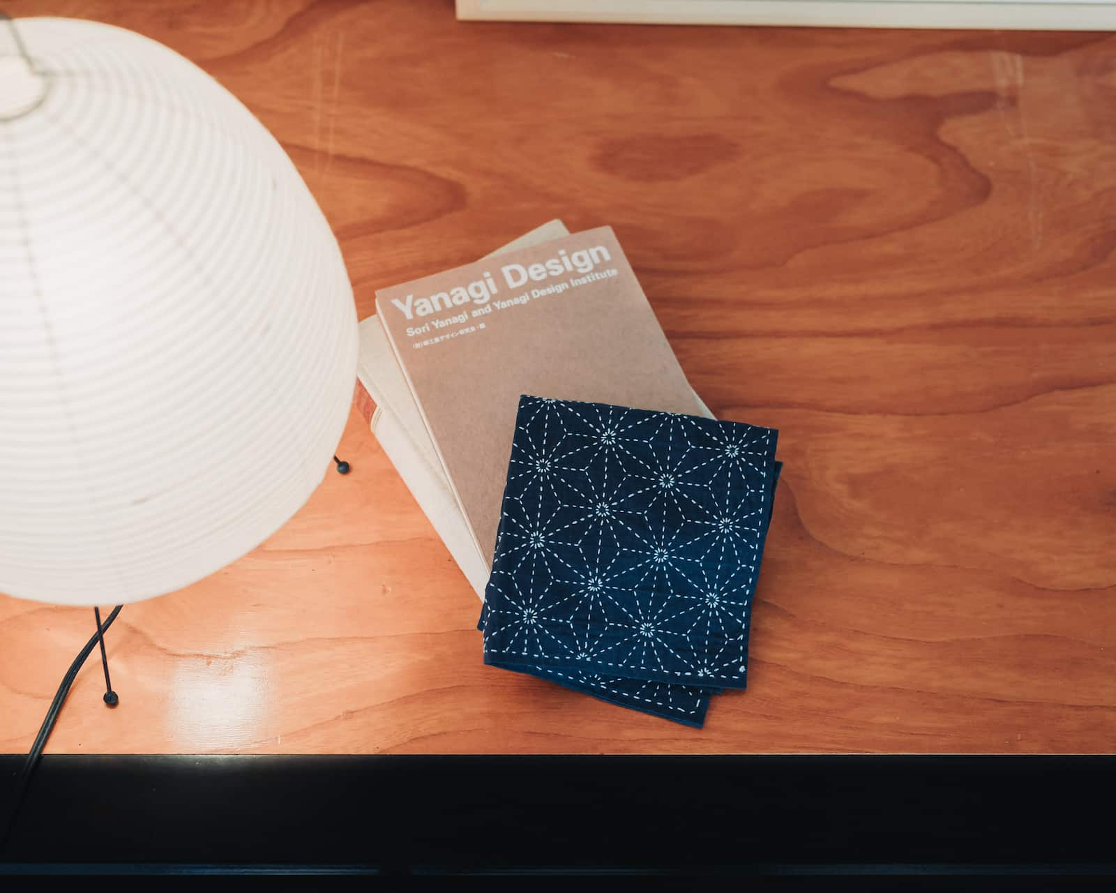 A sashiko kitchen towel in indigo with light blue thread drawing the asanoha pattern lying on a book next to a Japanese lantern