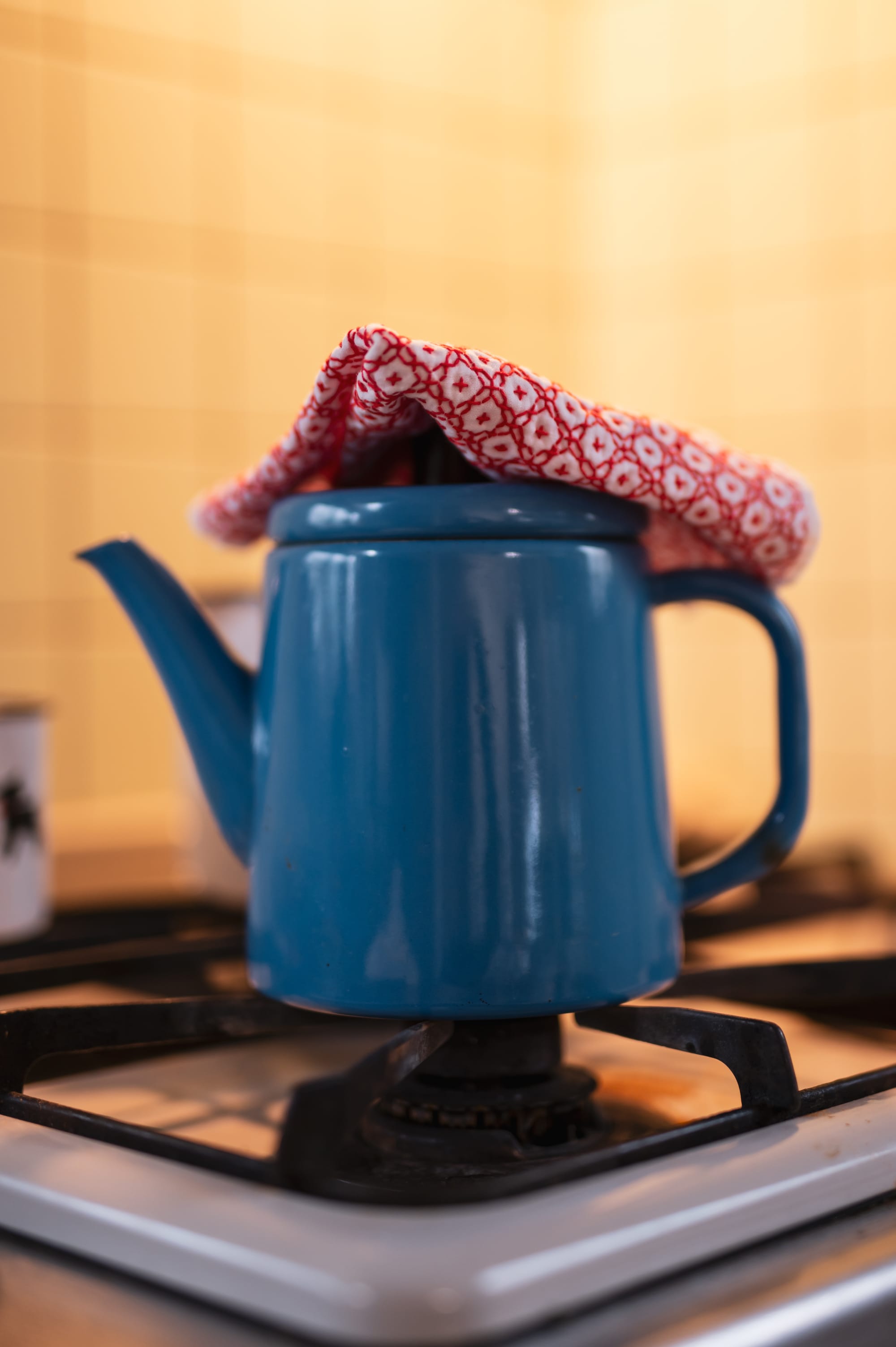 A blue enamel teapot on a gas stove with a sashiko kitchen cloth on top