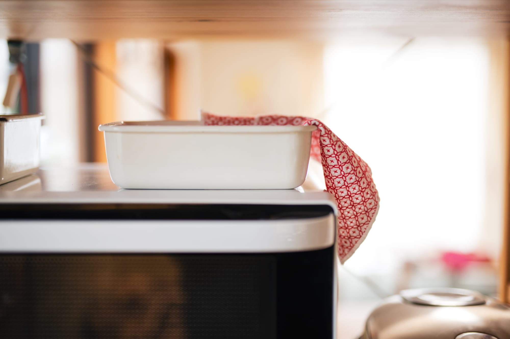 A sashiko kitchen cloth with the jūjihanazashi pattern in red on white lying on top of an enamel bowl in a cupboard.