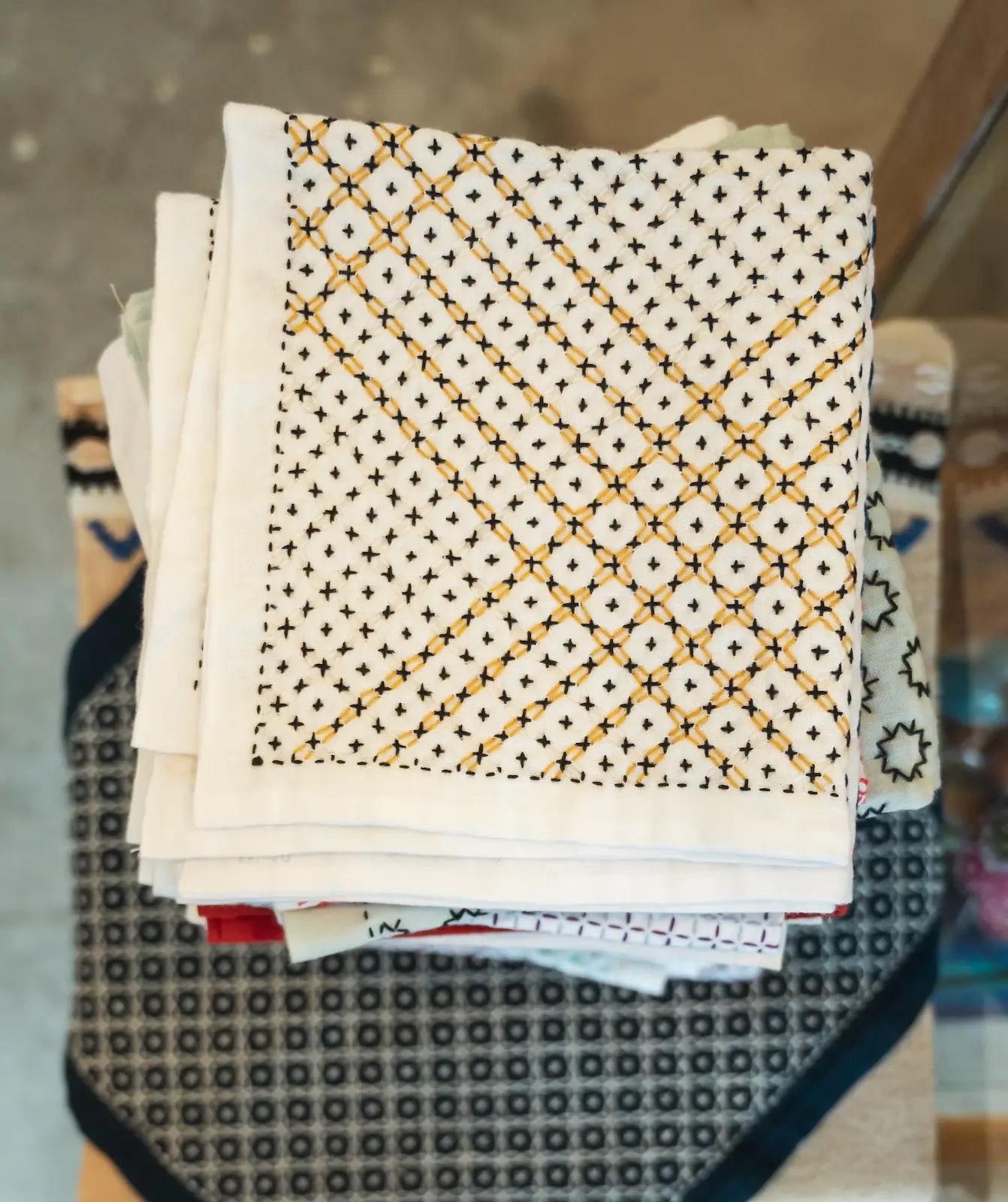 Sashiko kitchen cloths in a pile, the topmost with the jujihanazashi pattern in white, indigo and brown thread.