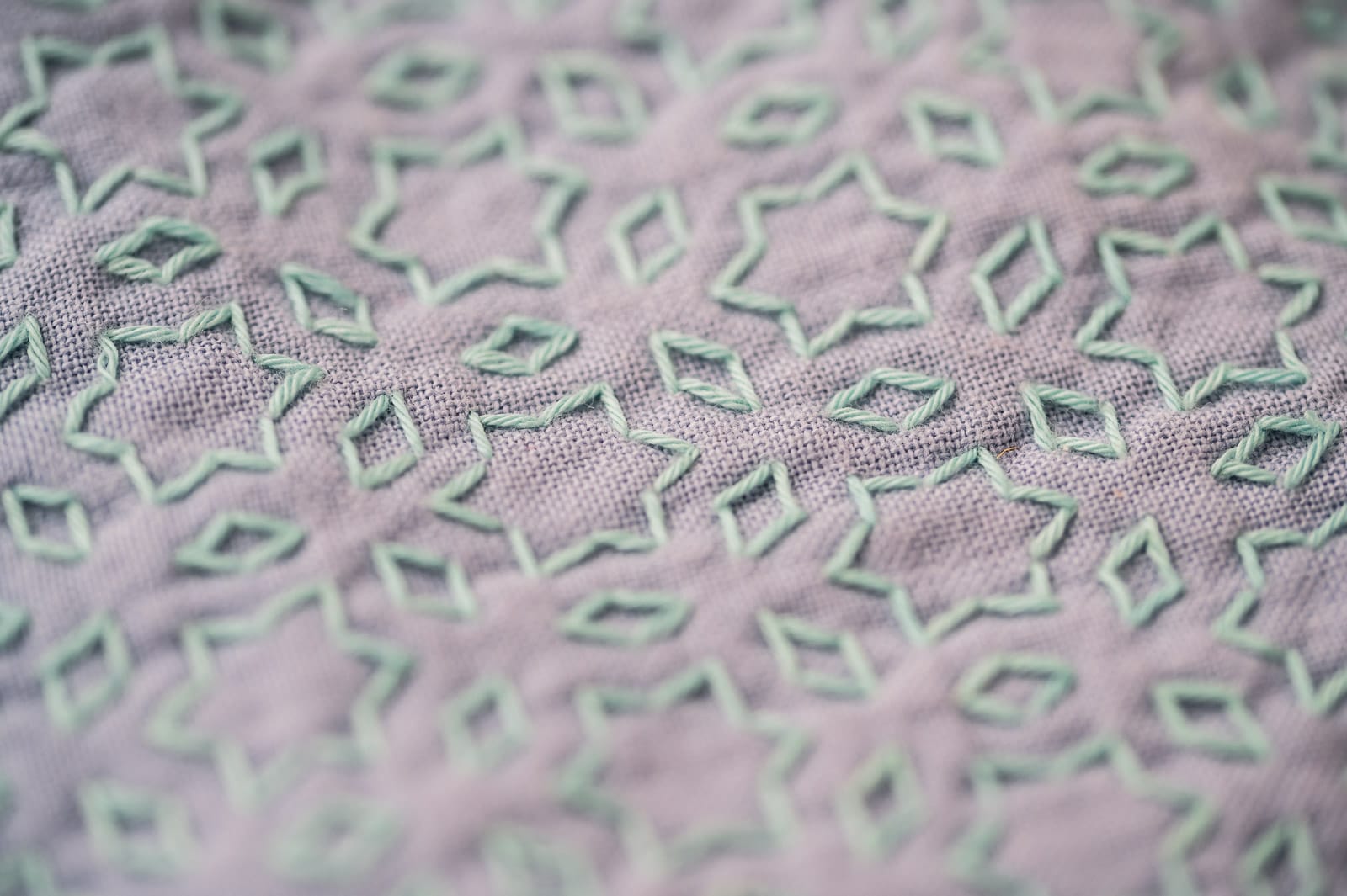 Sashiko pattern "hoshi to mitsubishi" in pale mint green thread on mauve fabric close up.