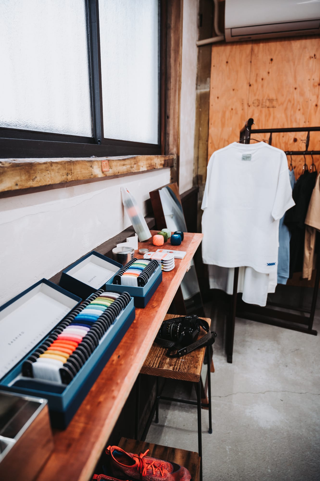 A shelf with Daruma thread displayed and sashiko shirts hanging in the background.