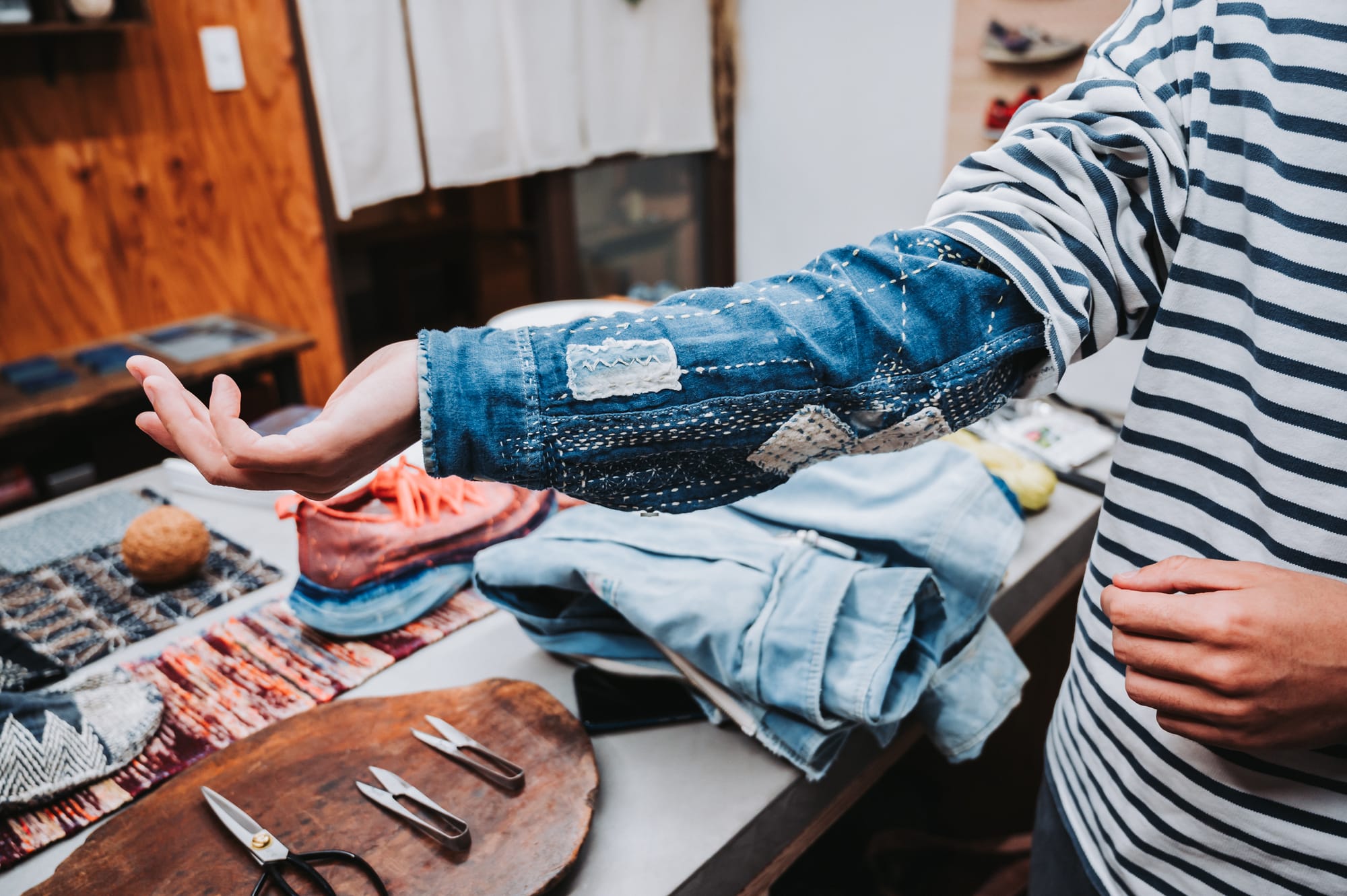 A person showing the sleeve of a denim shirt that was mended with sashiko in white thread.