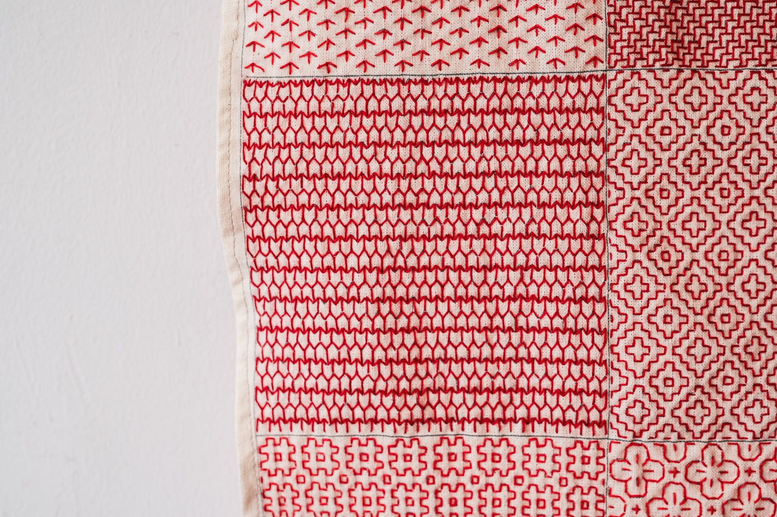 A hitomezashi version of the sashiko pattern yabane stitched in red thread on natural white fabric surrounded by other sashiko patterns