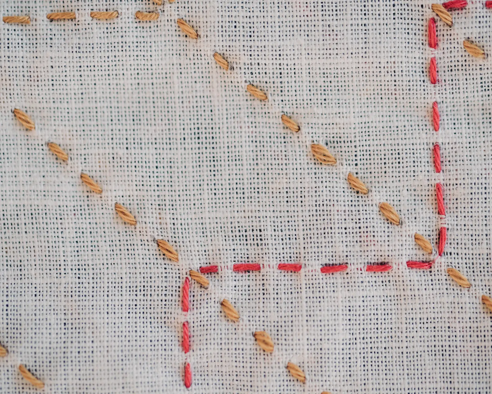 The yabane sashiko pattern in mustard and red thread on white fabric