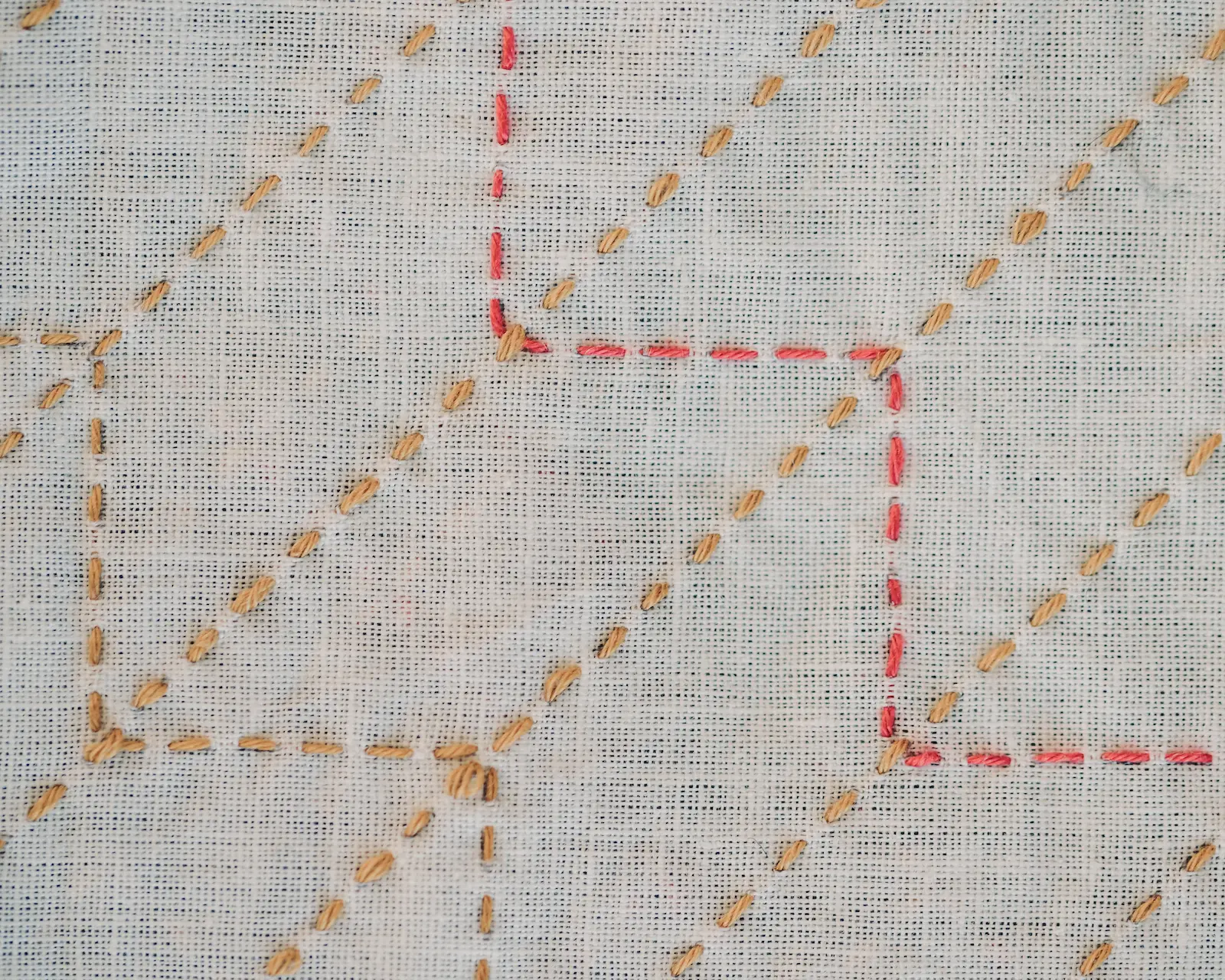 The yabane sashiko pattern in mustard and red thread on white fabric