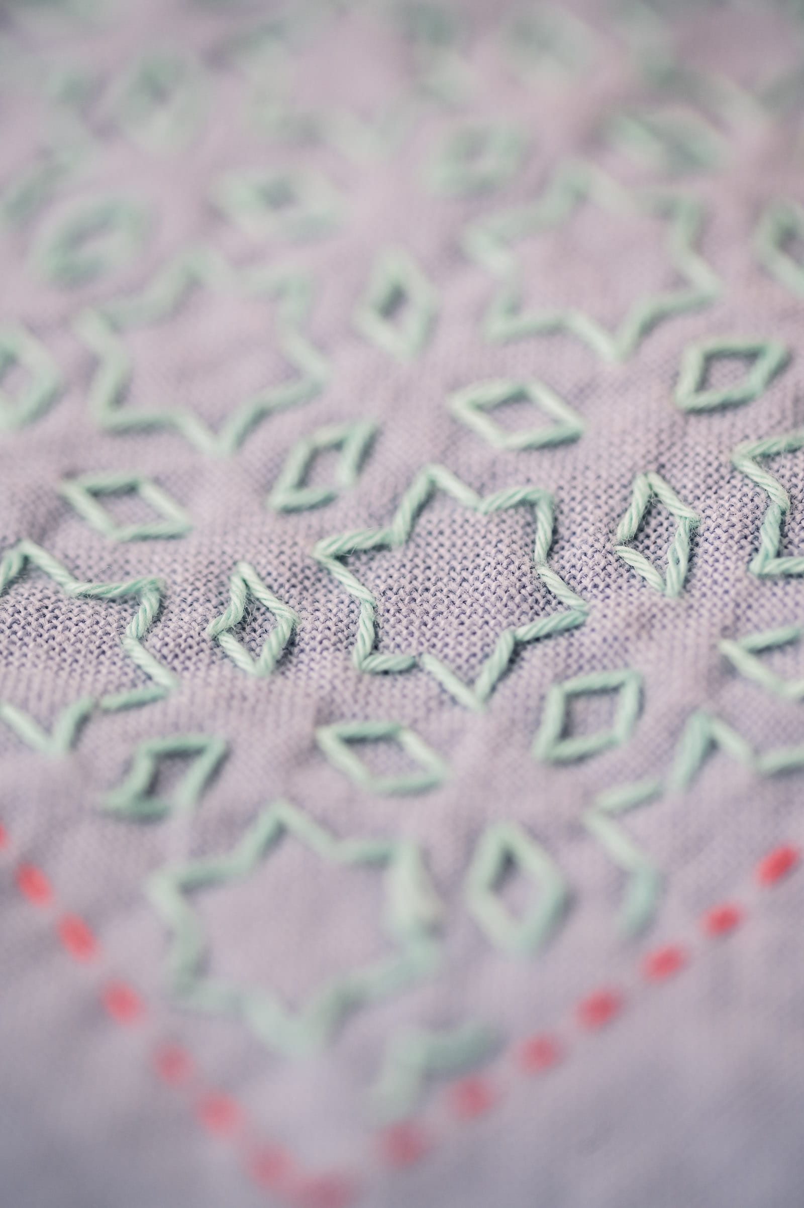 Sashiko pattern "hoshi to mitsubishi" in pale mint green thread on mauve fabric with a red frame close-up.