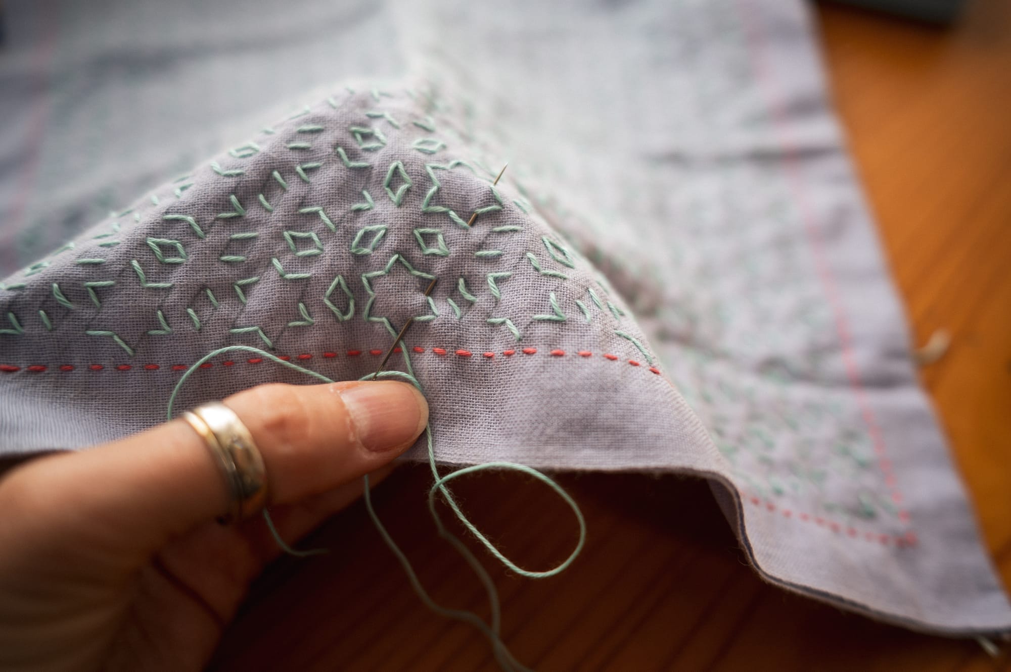 Sashiko pattern "hoshi to mitsubishi" in pale mint green thread on mauve fabric showing the needle carrying several stitches.