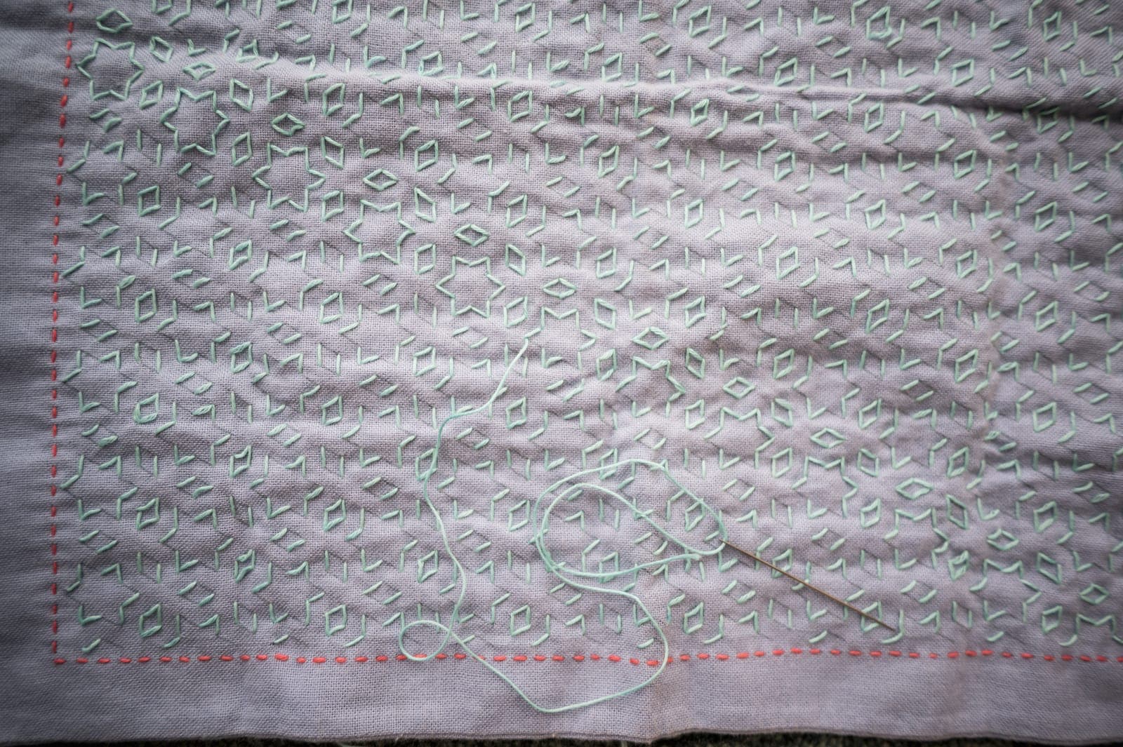 Sashiko pattern "hoshi to mitsubishi" in pale mint green thread on mauve fabric in the process of stitching.